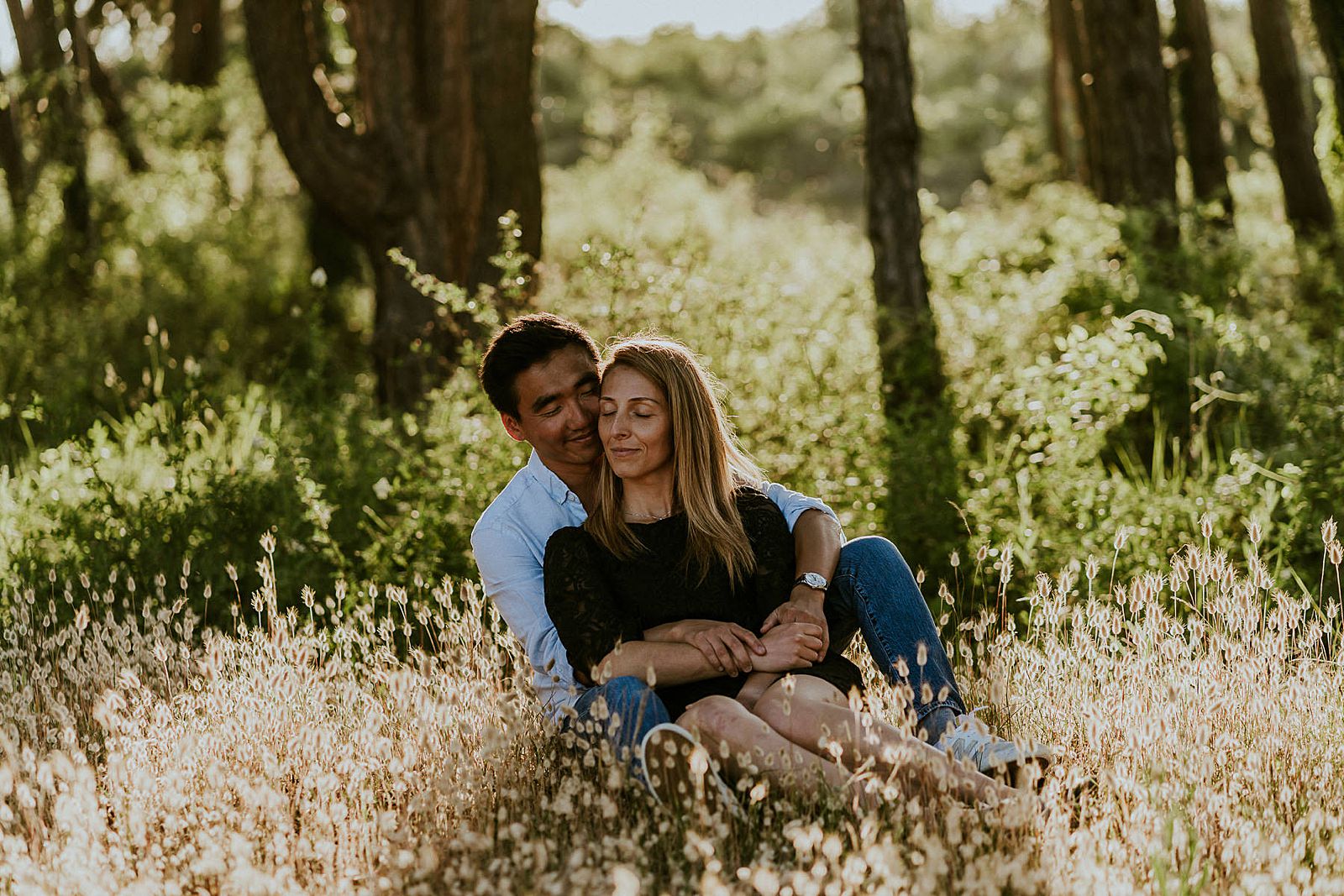 couple enlacé assis dans un champ de chatons à la golden hour